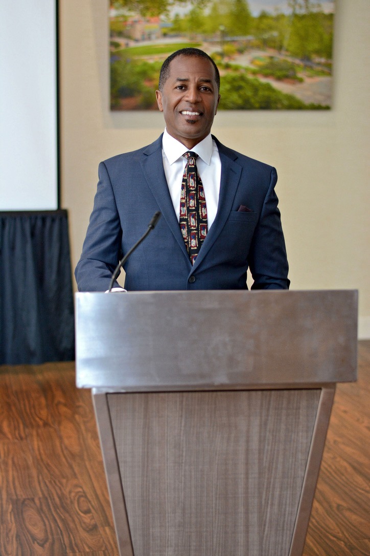 A confident speaker in a suit stands at a podium