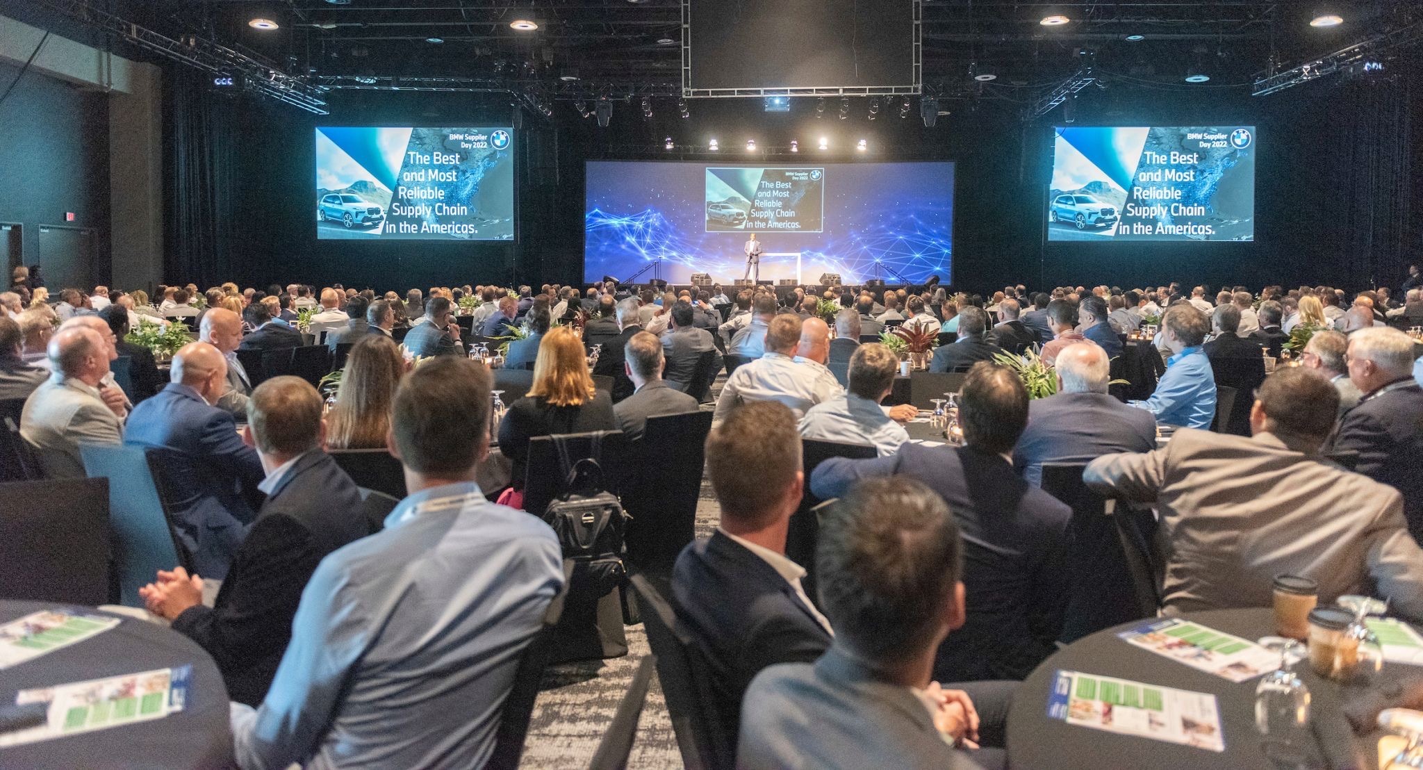 A large audience at an event focuses on a speaker and presentation