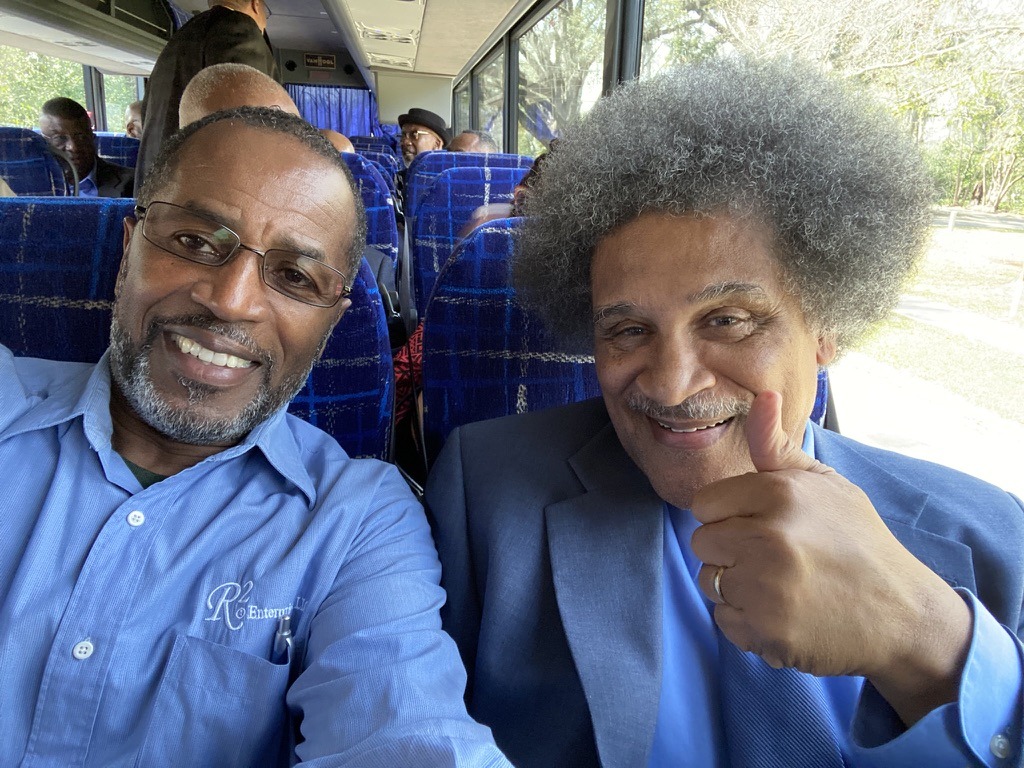 Two smiling men sit together on a bus