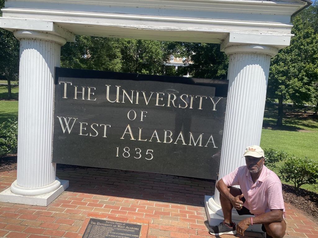 A visitor poses beside the sign for the University of West Alabama